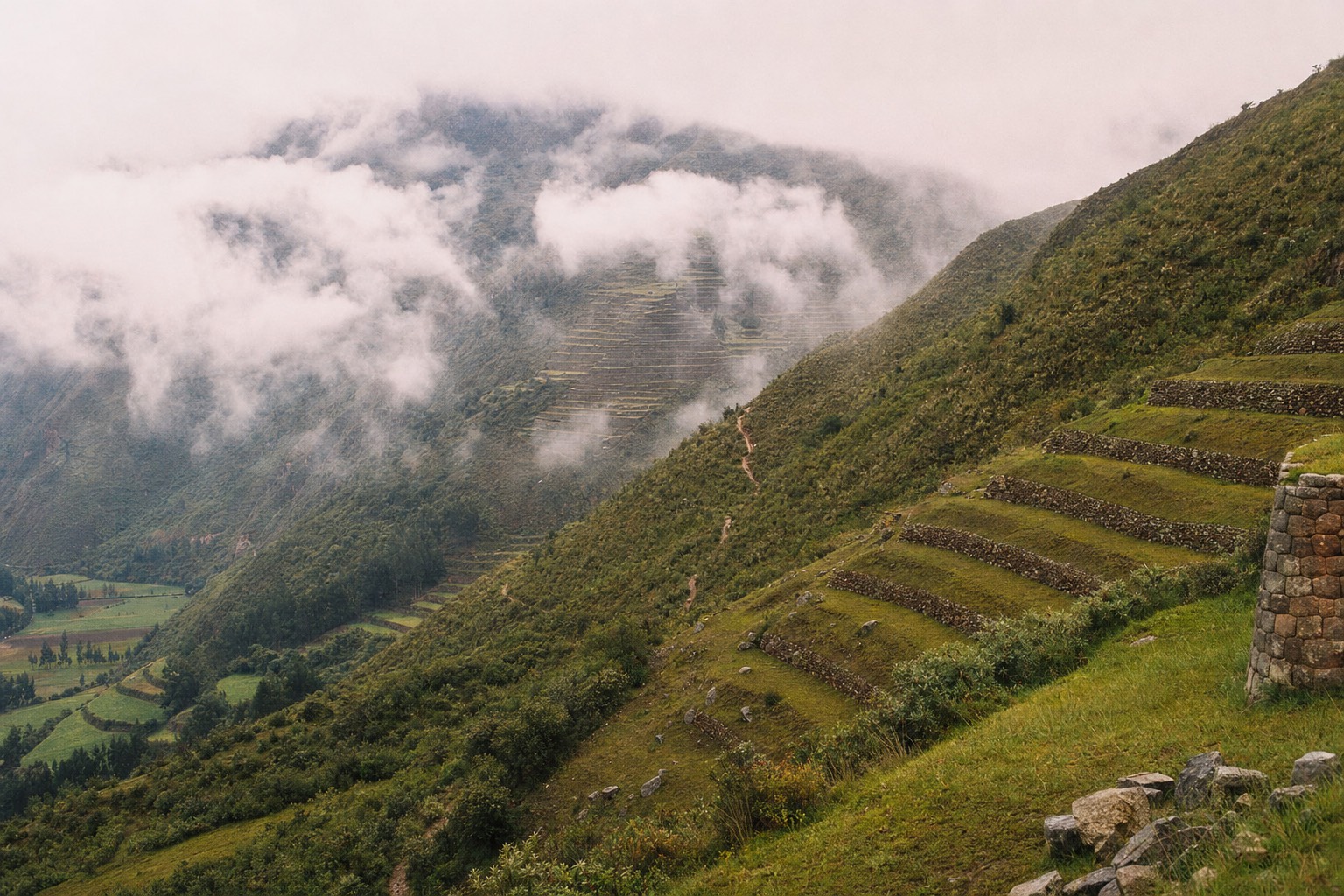 Terraced green mountainside in Peru's Sacred Valley under early morning cloud