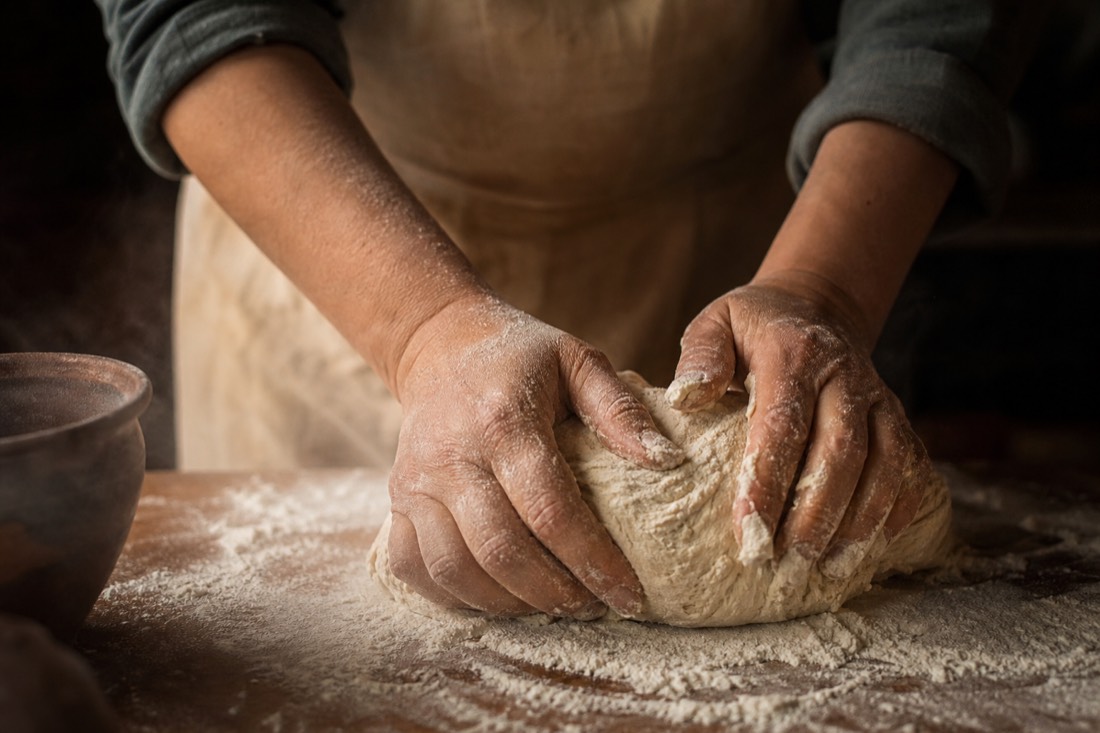 Hands kneading bread dough on a floured wooden counter in warm kitchen light