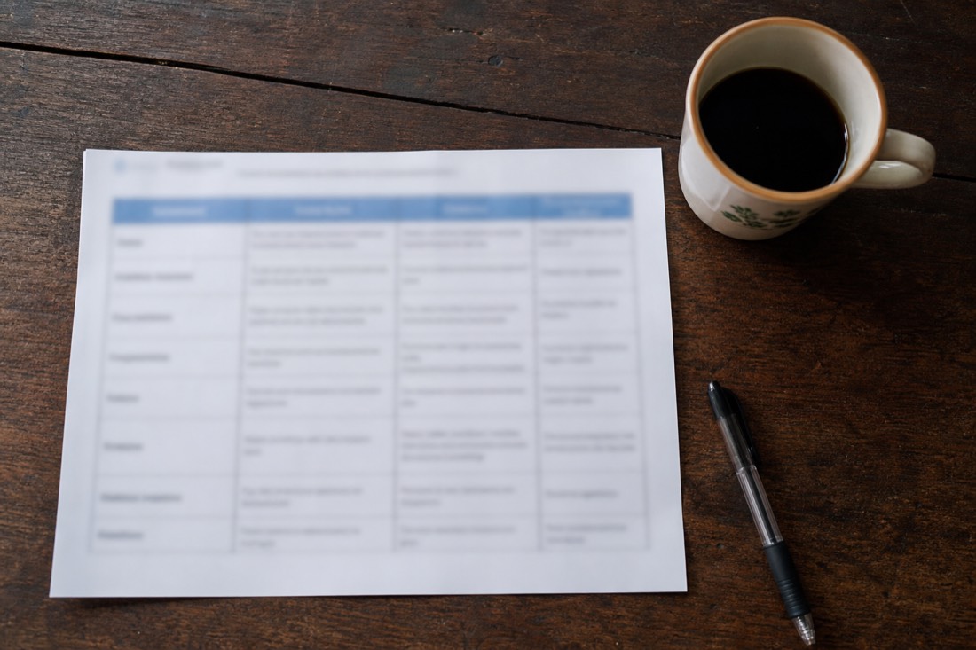 Overhead view of a printed comparison table, coffee cup and pen on a dark wooden table