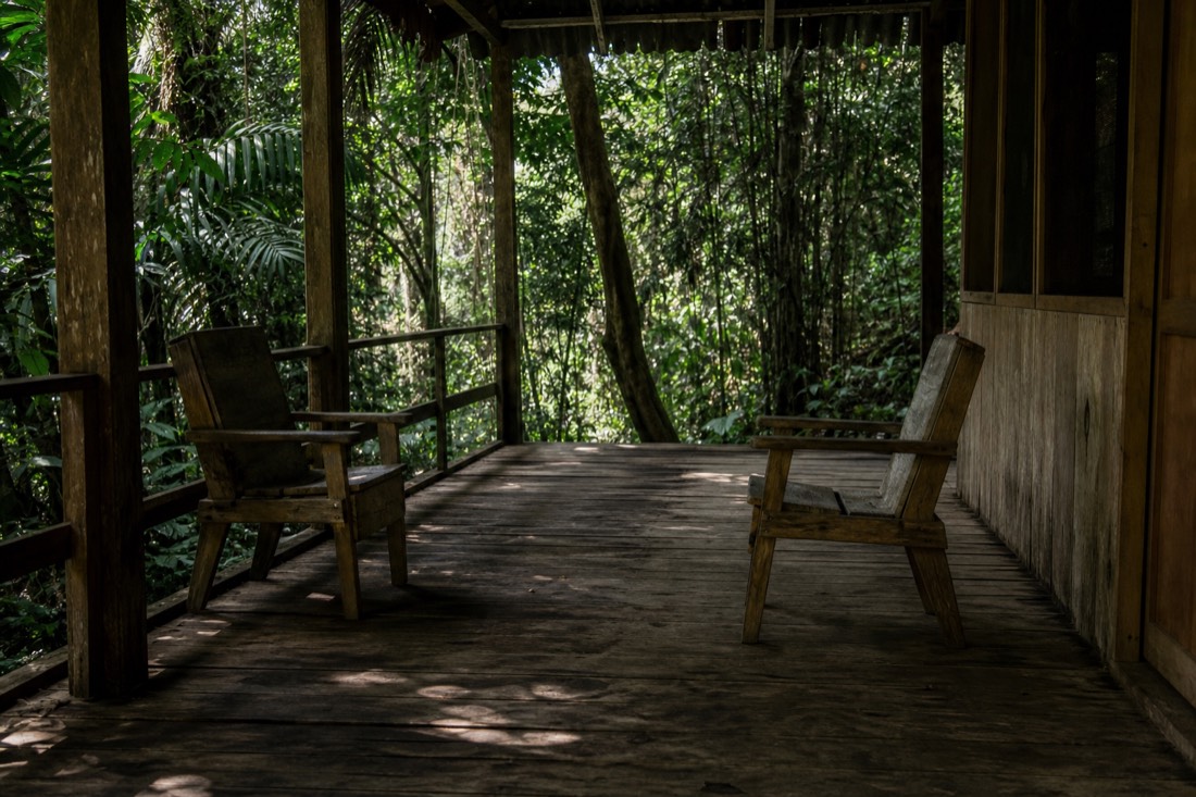 Two empty chairs facing each other on a rustic wooden porch in jungle shade