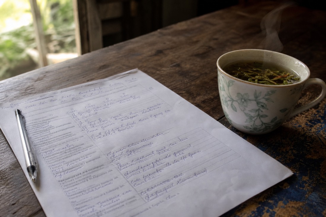 Close-up of a handwritten intake questionnaire on a rough wooden table beside a cup of herbal tea