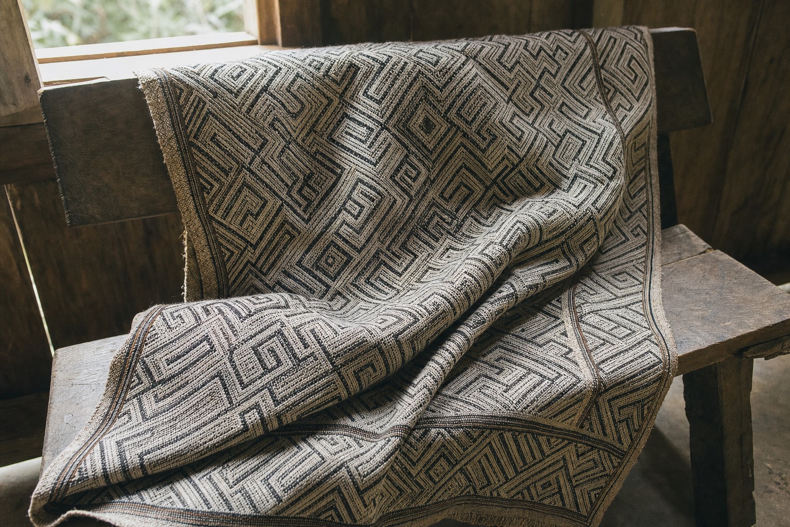 Shipibo geometric textile in white and black draped over a wooden bench in soft light