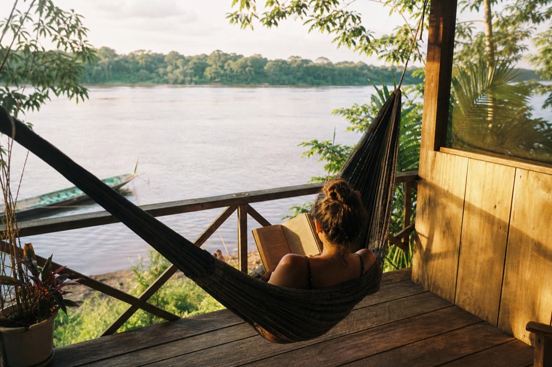 Woman reading in a hammock on a retreat veranda above a calm river in afternoon light