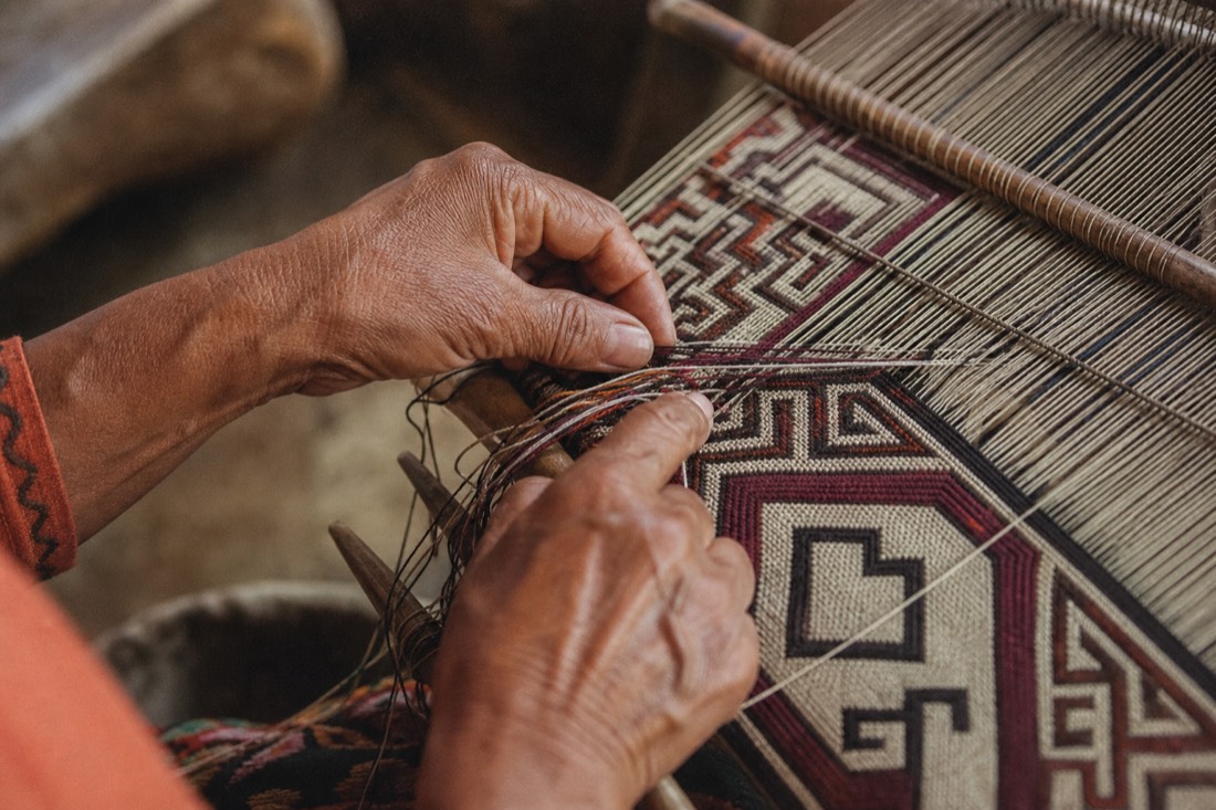 Hands weaving an intricate geometric patterned textile in natural light, Shipibo-style design, Pucallpa region, no faces visible