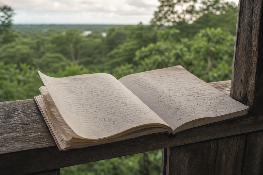 Weathered guest book lying open on a wooden veranda rail with pages ruffled by wind, writing illegible, rainforest beyond, Loreto region