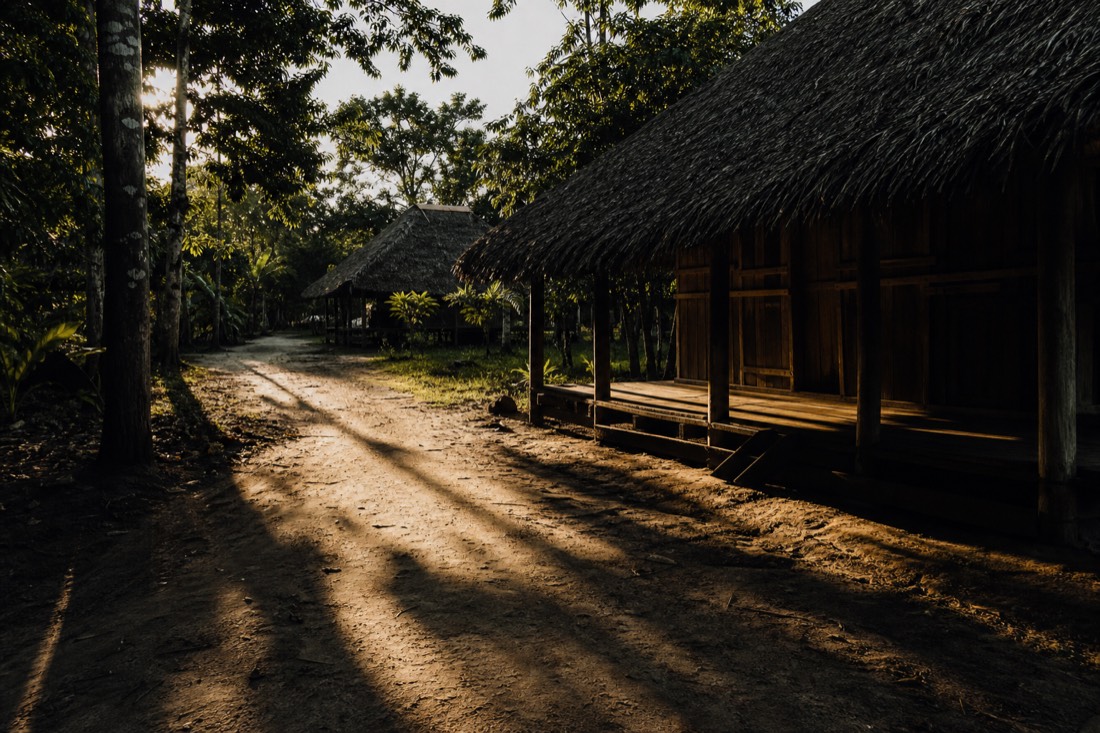 Long afternoon shadows crossing a bare footpath between jungle huts on a quiet rest day