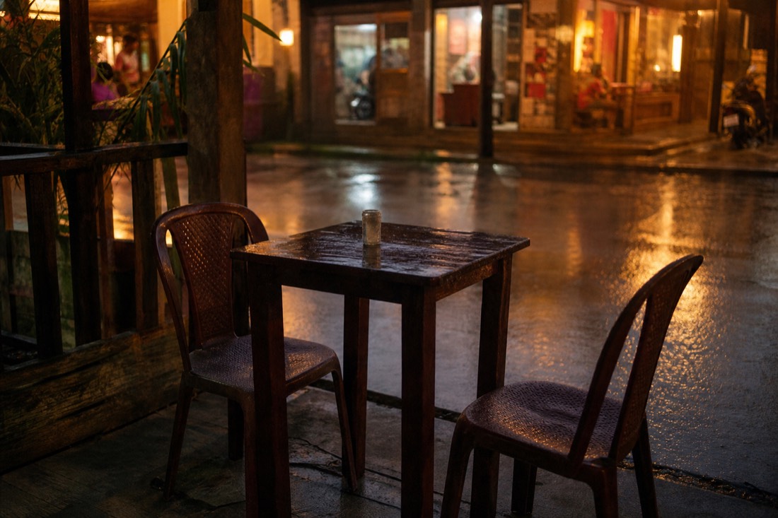 Two plastic chairs at a small streetside cafe table in a jungle town at dusk