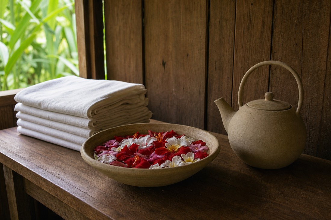 Retreat welcome table with folded linens, a bowl of flower-bath petals and a ceramic kettle in soft daylight