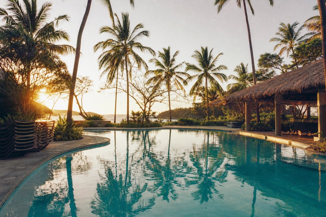 Empty resort pool ringed by palm trees at dawn on a quiet tropical property in Guanacaste