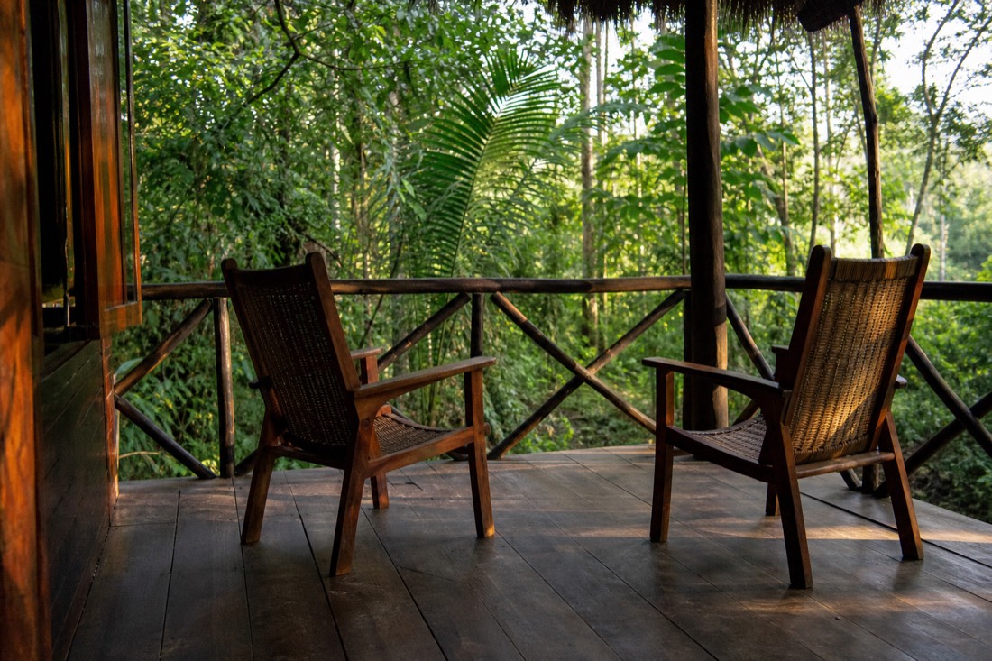 Two empty wooden chairs facing each other on a jungle veranda in late afternoon light