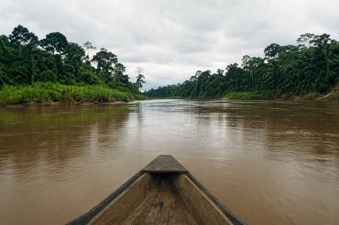 Wooden boat traveling a wide brown Amazon river channel between forested banks near Tamshiyacu, Peru